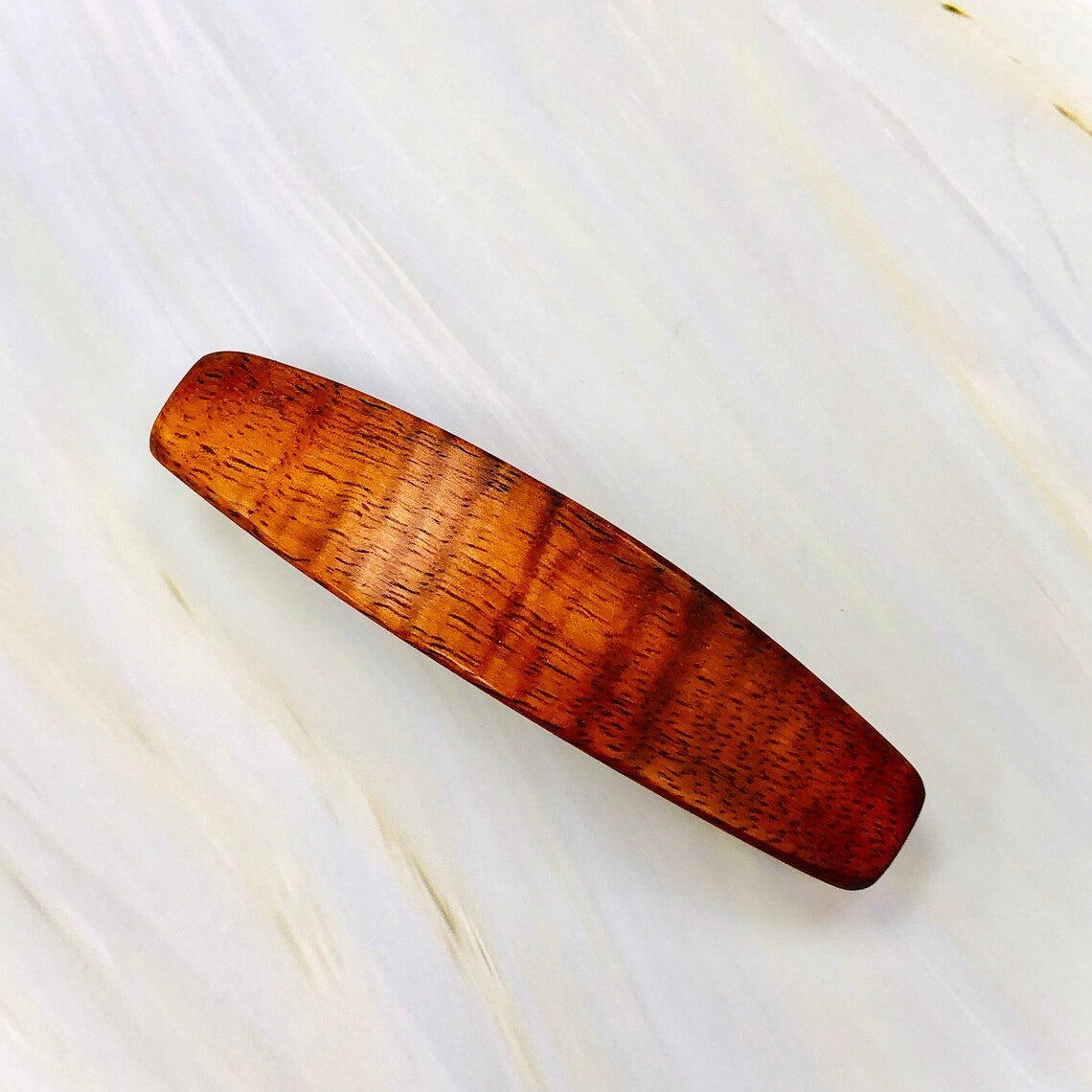 May include: A wooden hair clip with a reddish-brown color and a smooth, polished finish.