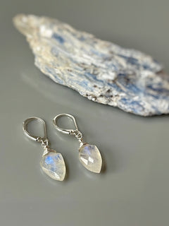 May include: A pair of silver dangle earrings with teardrop shaped moonstone gemstones. The moonstone is a light iridescent white with blue and green flashes.