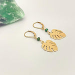May include: Gold earrings with green gemstone accents and a leaf design. The earrings are dangling and have a hook closure.