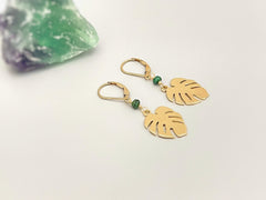 May include: Gold earrings with green gemstone accents and a leaf design. The earrings are dangling and have a hook closure.