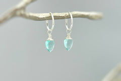 May include: A pair of silver hoop earrings with light blue teardrop-shaped gemstones hanging from them.
