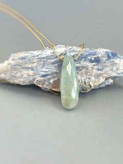 May include: A teardrop shaped light green gemstone pendant on a gold chain.