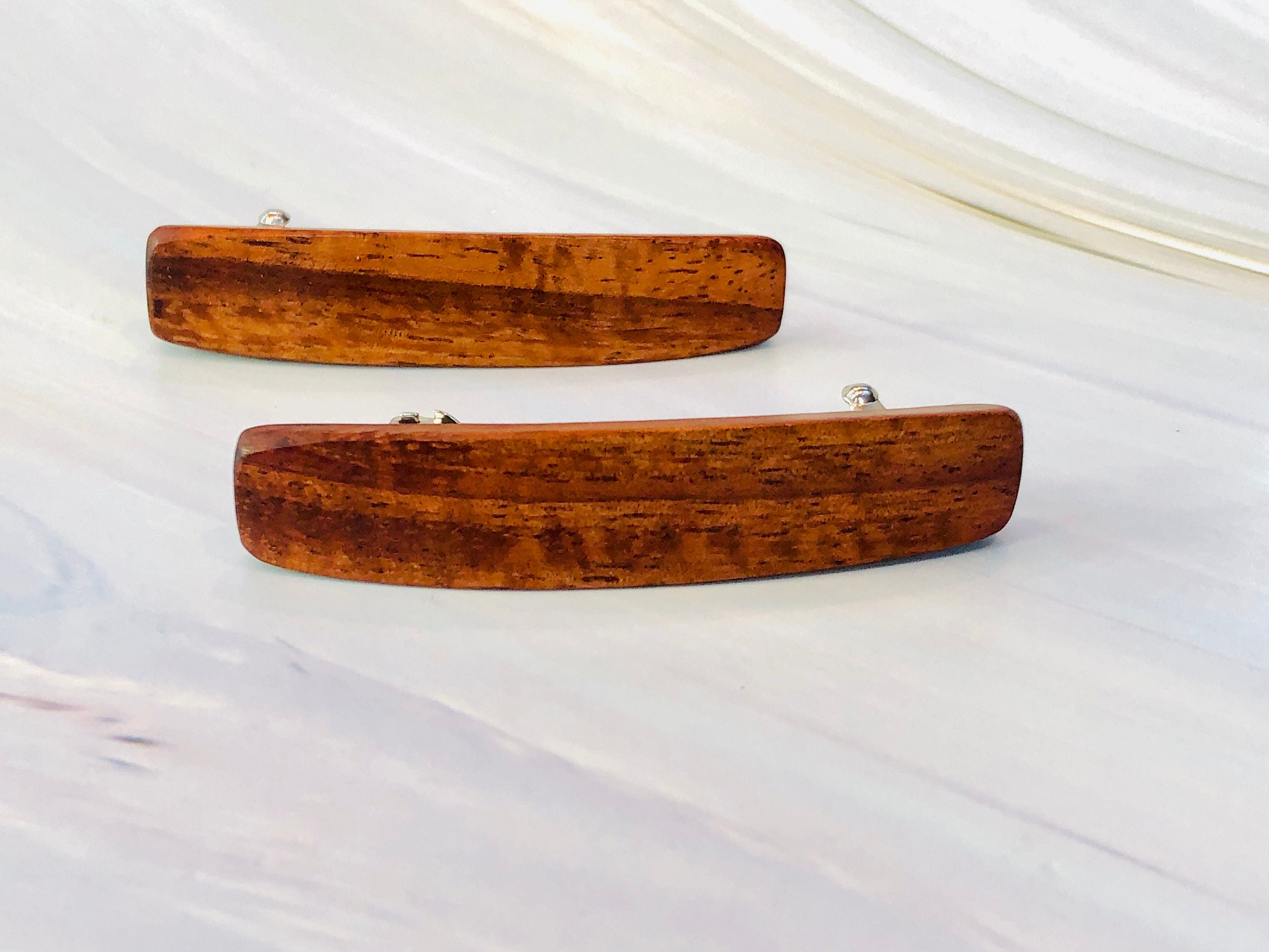 May include: Two wooden hair clips with silver metal clasps. The clips are brown and have a natural wood grain pattern.