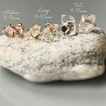 May include: Three pairs of clear quartz crystal earrings with gold wire wrapping. The earrings are arranged in a row from smallest to largest. The smallest earrings are labeled 'Medium 8-9mm', the middle earrings are labeled 'Large 9-10mm', and the largest earrings are labeled 'XL 11-13mm'.