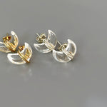 May include: Two pairs of clear crystal earrings with gold accents. The earrings are shaped like crescent moons and are designed to be worn as studs.