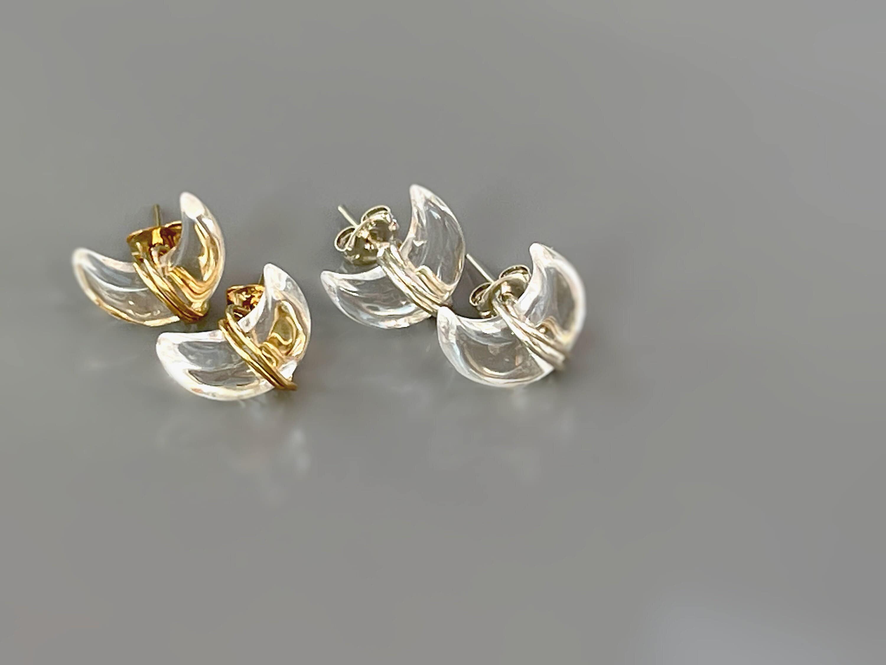 May include: Two pairs of clear crystal earrings with gold accents. The earrings are shaped like crescent moons and are designed to be worn as studs.