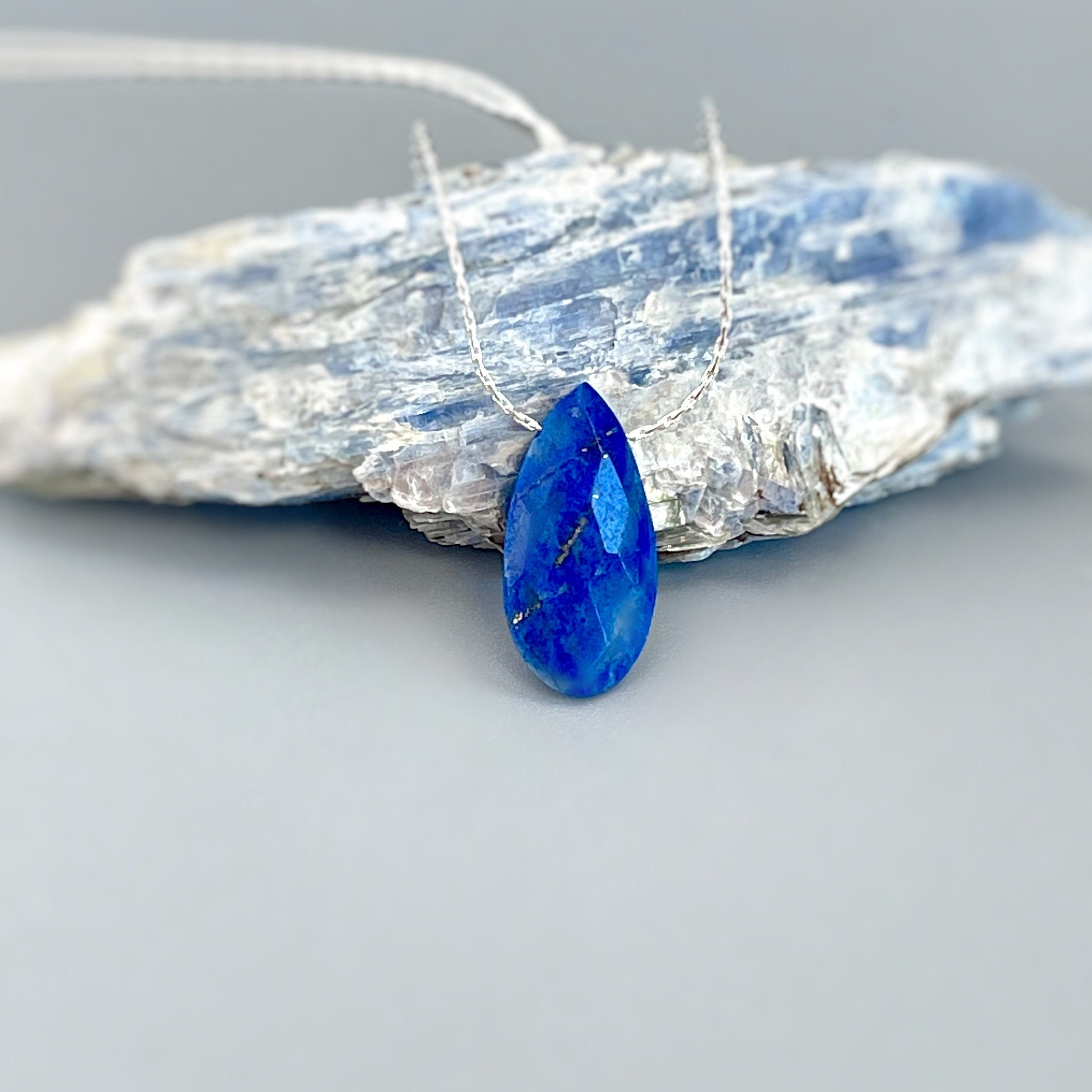 May include: A silver chain necklace with a teardrop-shaped blue lapis lazuli pendant