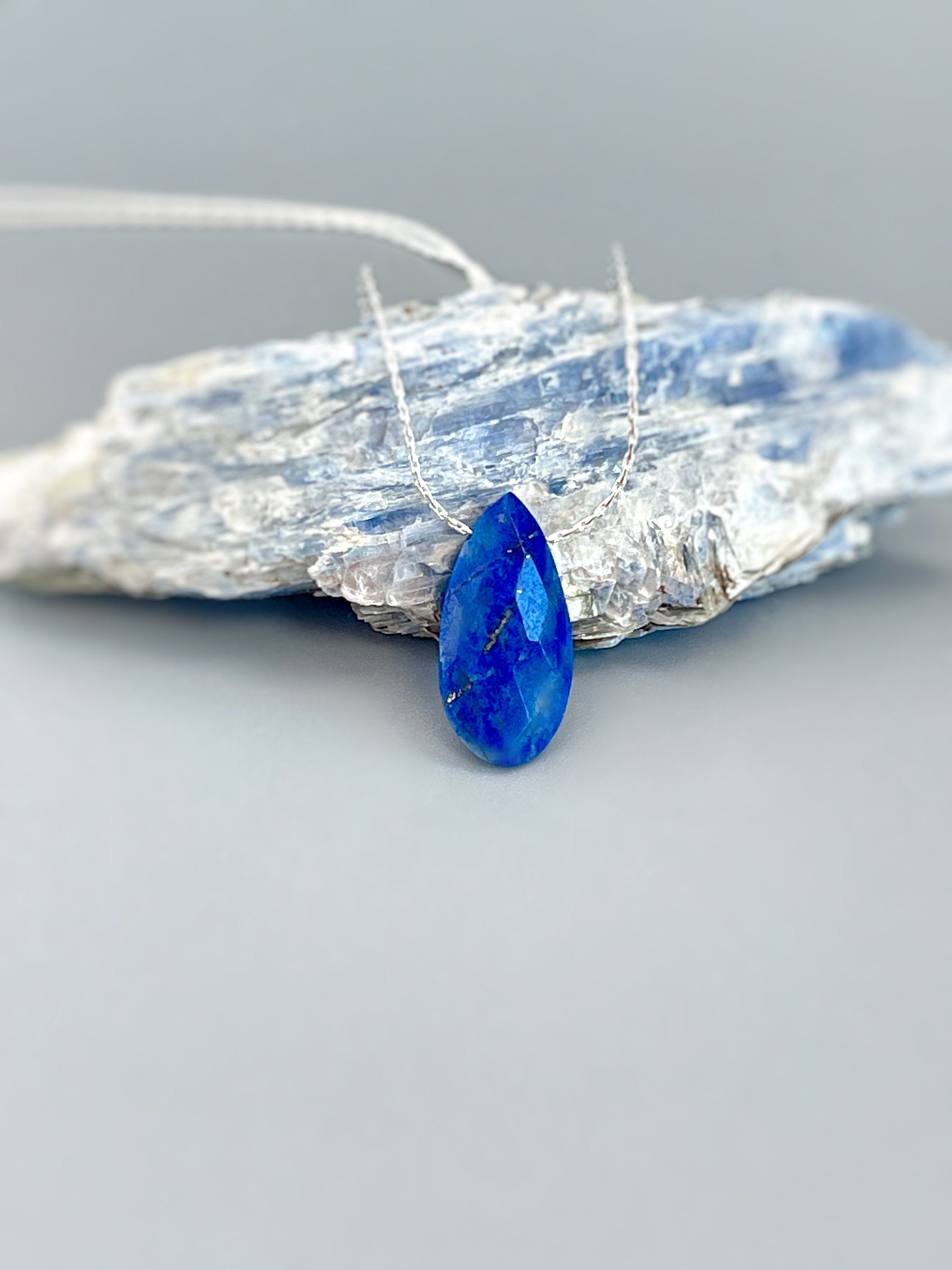 May include: A silver chain necklace with a teardrop-shaped blue lapis lazuli pendant