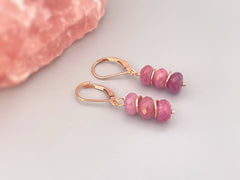 May include: A pair of dangle earrings with rose gold hooks and pink gemstone beads. The beads are faceted and have a gradient of pink shades.
