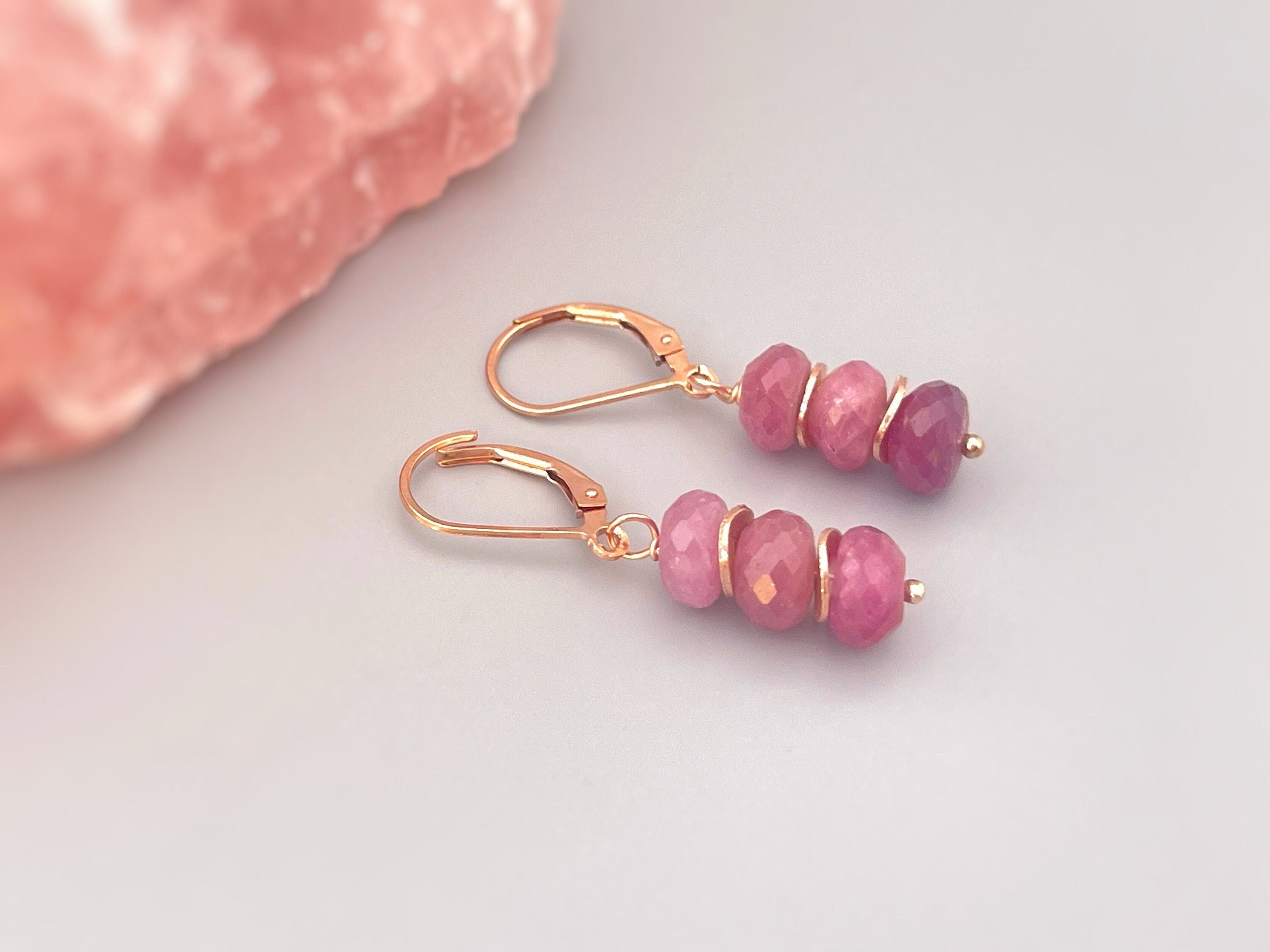 May include: A pair of dangle earrings with rose gold hooks and pink gemstone beads. The beads are faceted and have a gradient of pink shades.