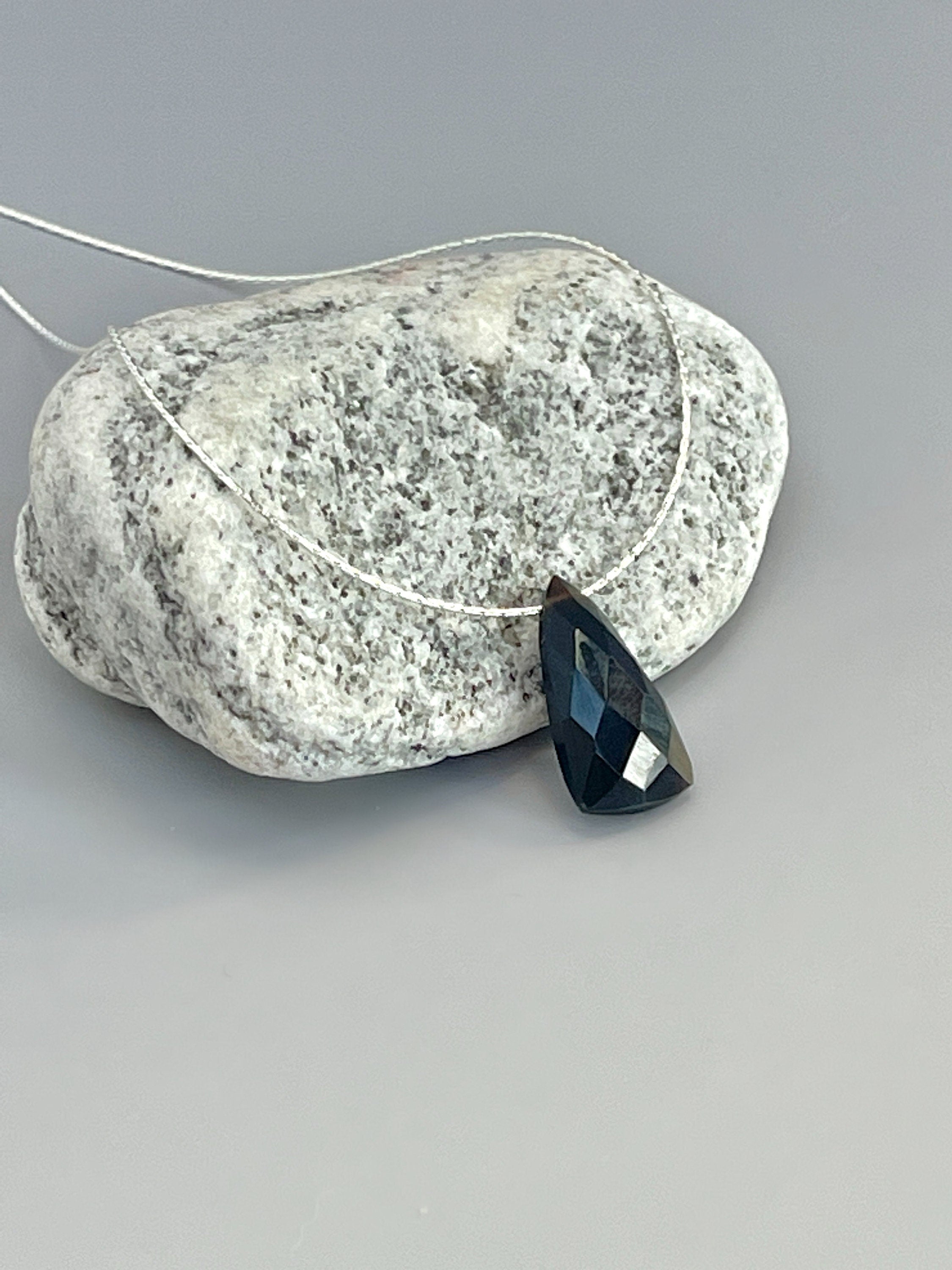 May include: A black gemstone pendant on a silver chain. The gemstone is faceted and has a teardrop shape.