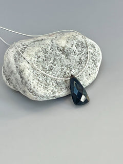 May include: A black gemstone pendant on a silver chain. The gemstone is faceted and has a teardrop shape.