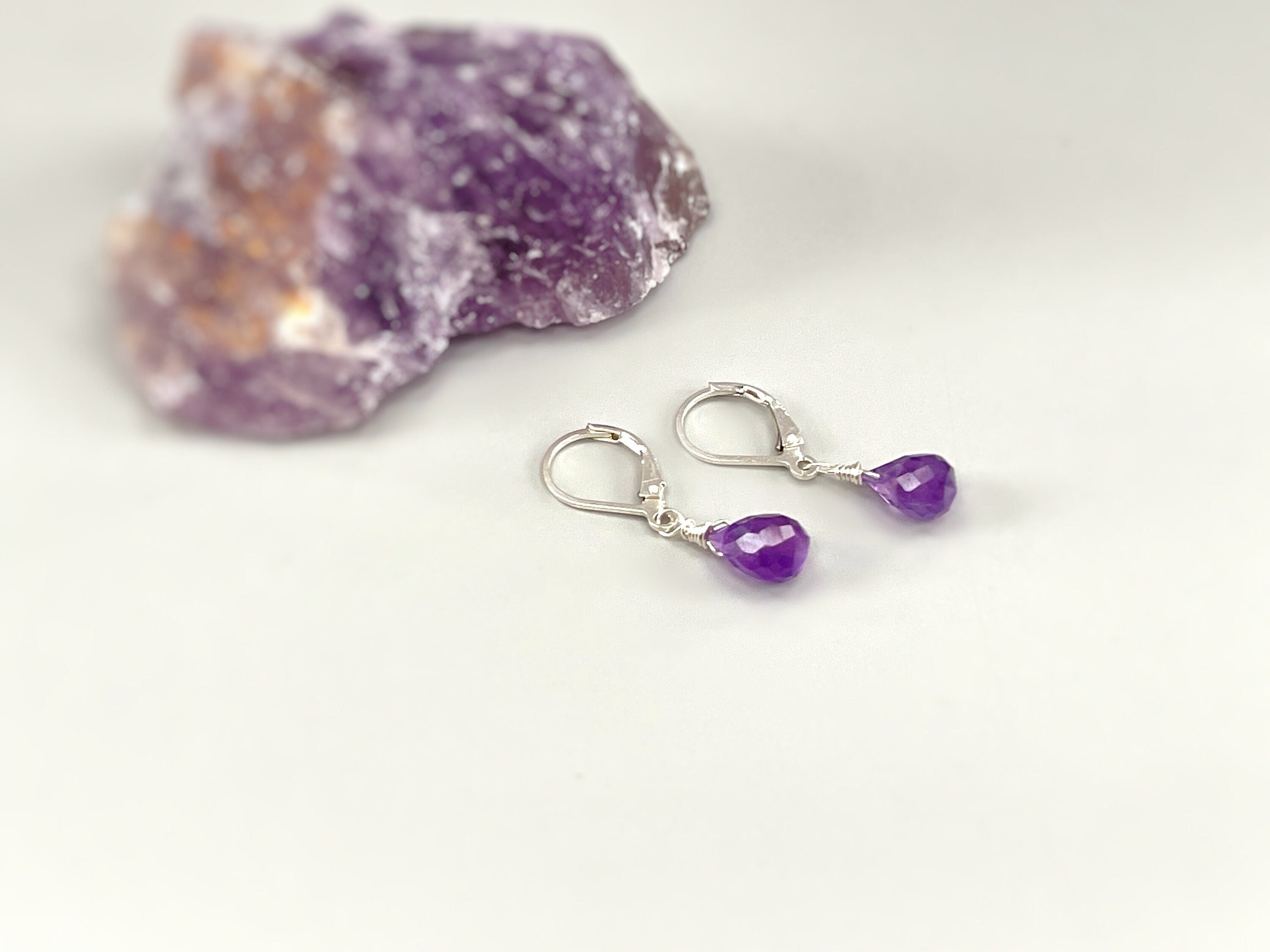 May include: A pair of silver earrings with purple amethyst teardrop stones. The earrings are dangling and have a wire wrapped around the stone.