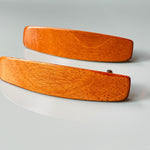 May include: Two wooden hair clips in a light brown color.  The clips are rectangular with slightly rounded edges and feature a smooth, polished finish. They appear to be made of a light-colored wood, possibly cherry or mahogany. The clips are simple and elegant in design, suitable for everyday use.