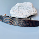 May include: A dark brown wood hair clip with a silver metal clasp. The wood has a striped pattern.