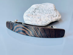 May include: A dark brown wood hair clip with a silver metal clasp. The wood has a striped pattern.