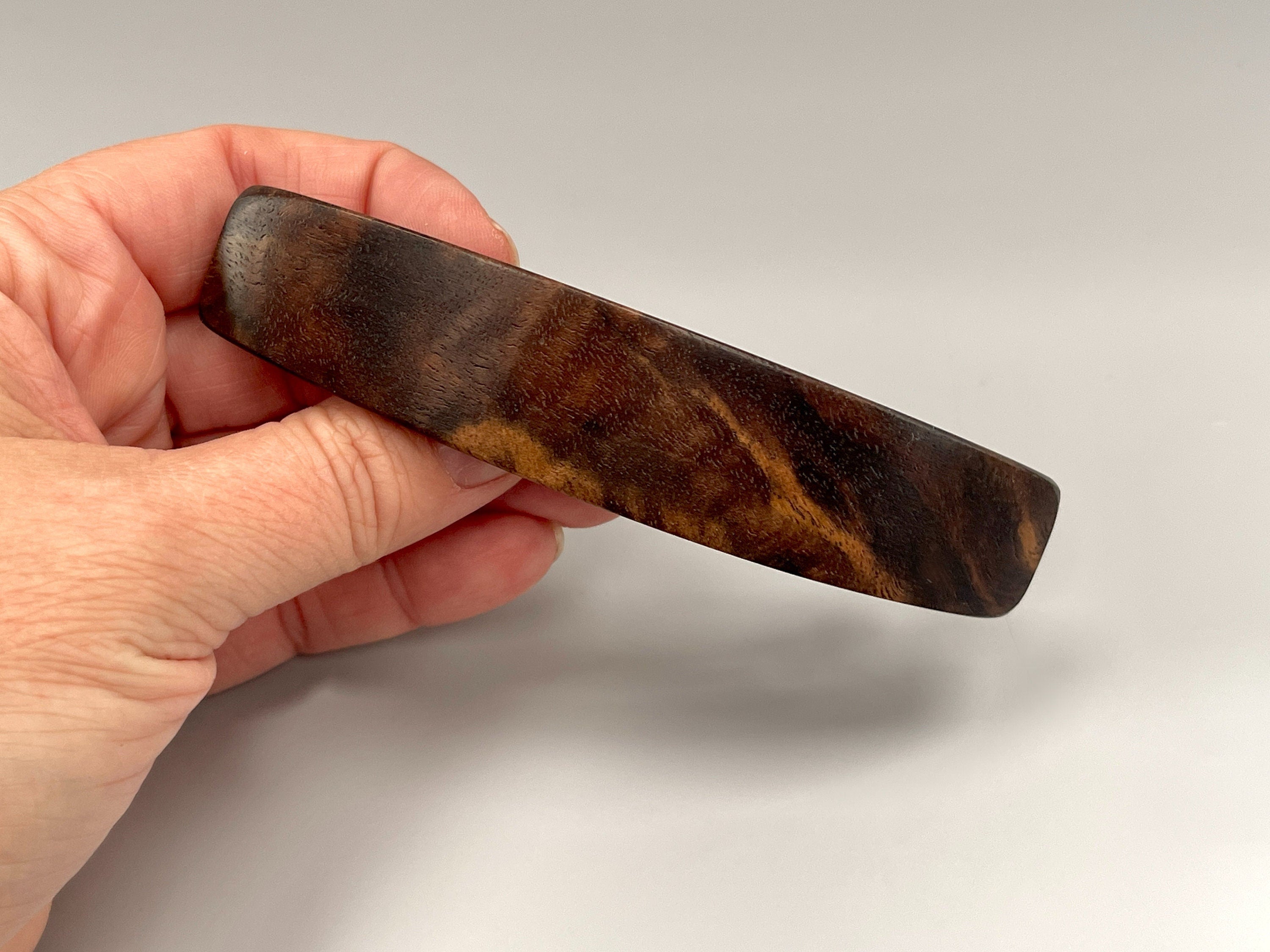 May include: A dark brown wooden hair clip with a smooth, polished finish.