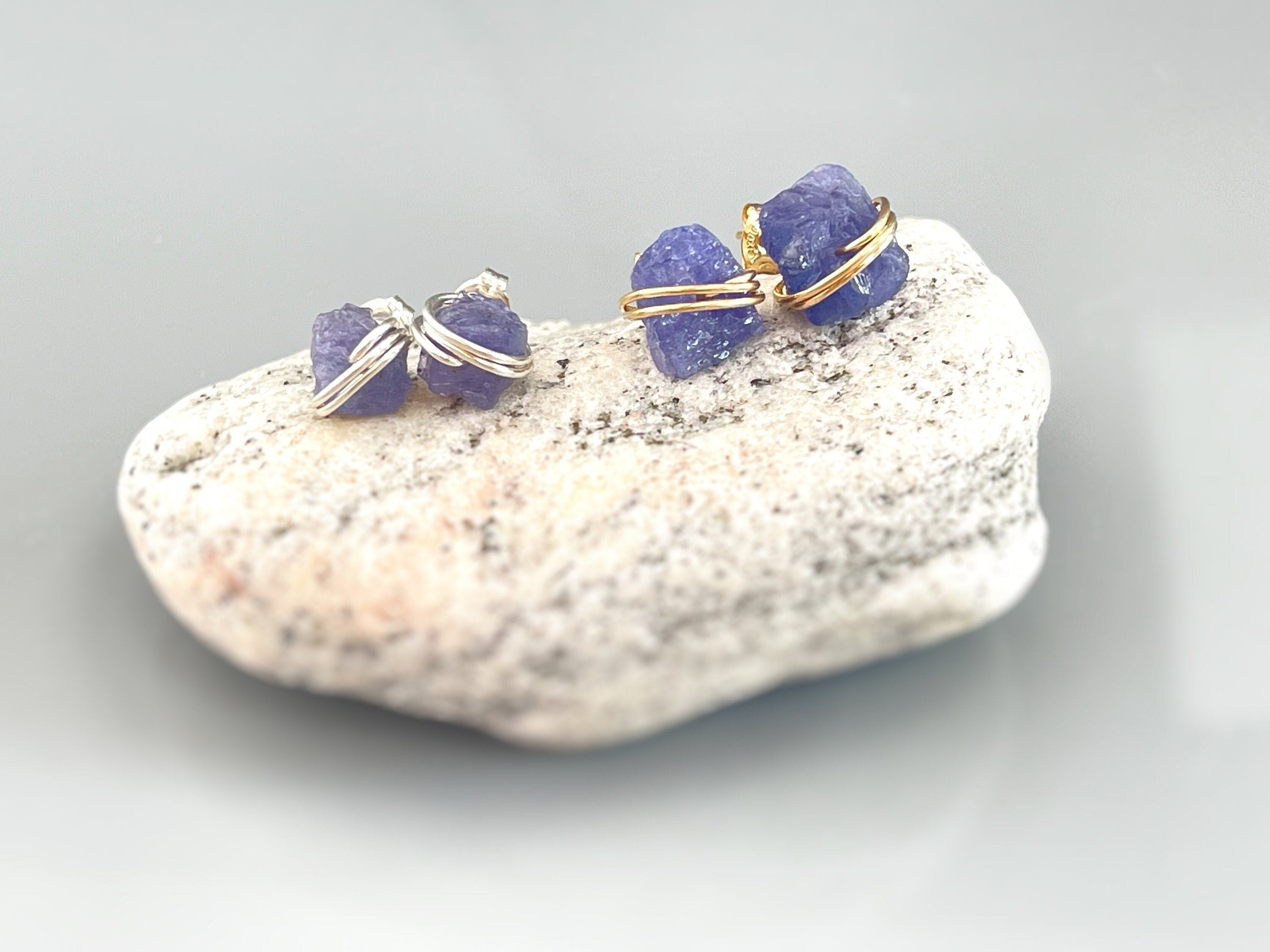 May include: Two pairs of earrings with purple gemstones wrapped in silver and gold wire.