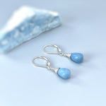 May include: A pair of silver teardrop earrings with light blue gemstone drops. The earrings have a simple design and are perfect for everyday wear.