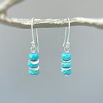 May include: Silver dangle earrings with turquoise blue beads and silver spacers. The earrings are hanging from a branch.