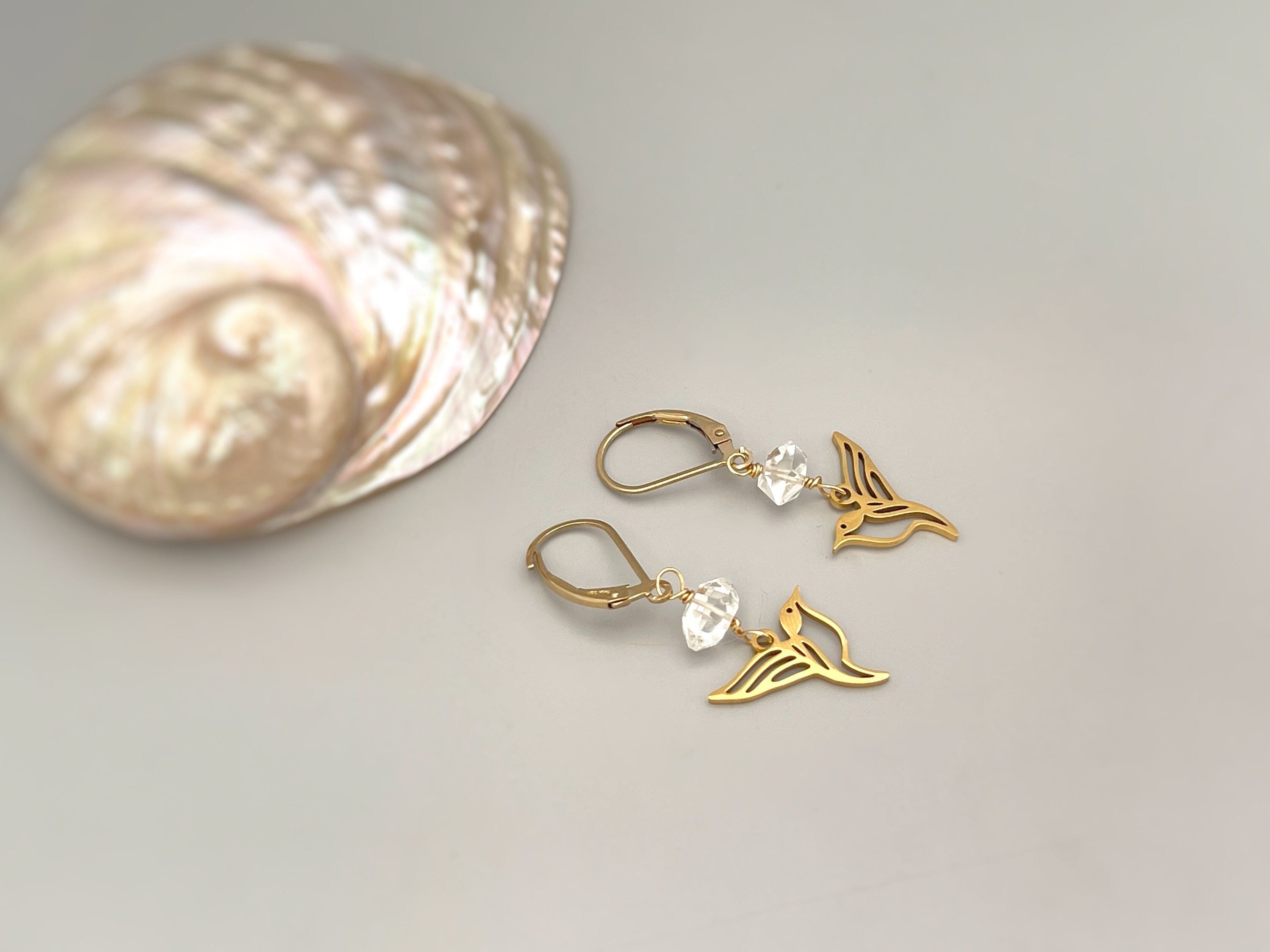 May include: A pair of gold earrings with clear crystal beads and a hummingbird design.
