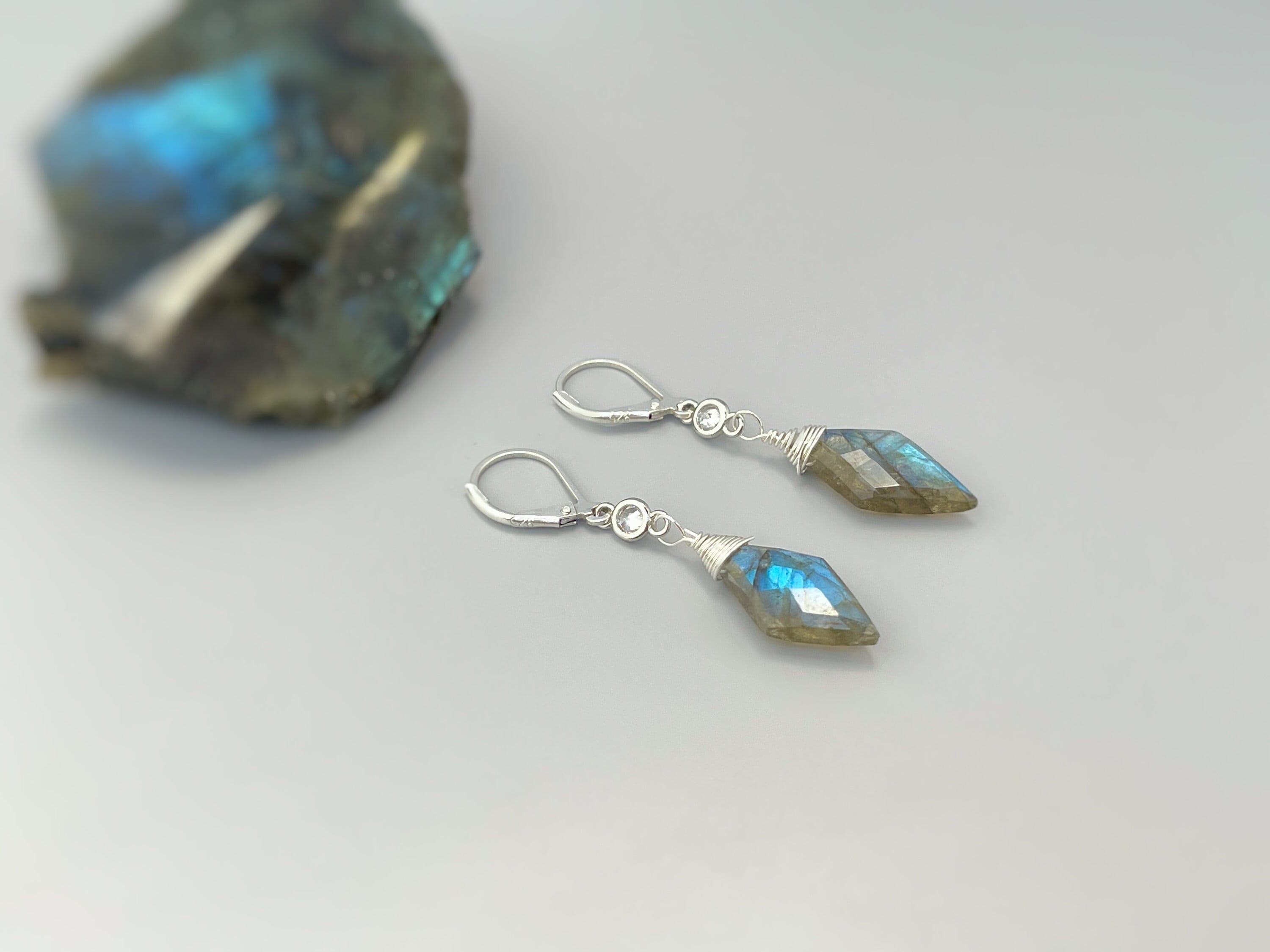May include: A pair of silver dangle earrings with a teardrop shaped blue-green labradorite gemstone on each earring. The earrings have a silver hook closure.