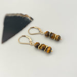 May include: Gold earrings with tiger's eye gemstone beads. The earrings have a lever back closure.
