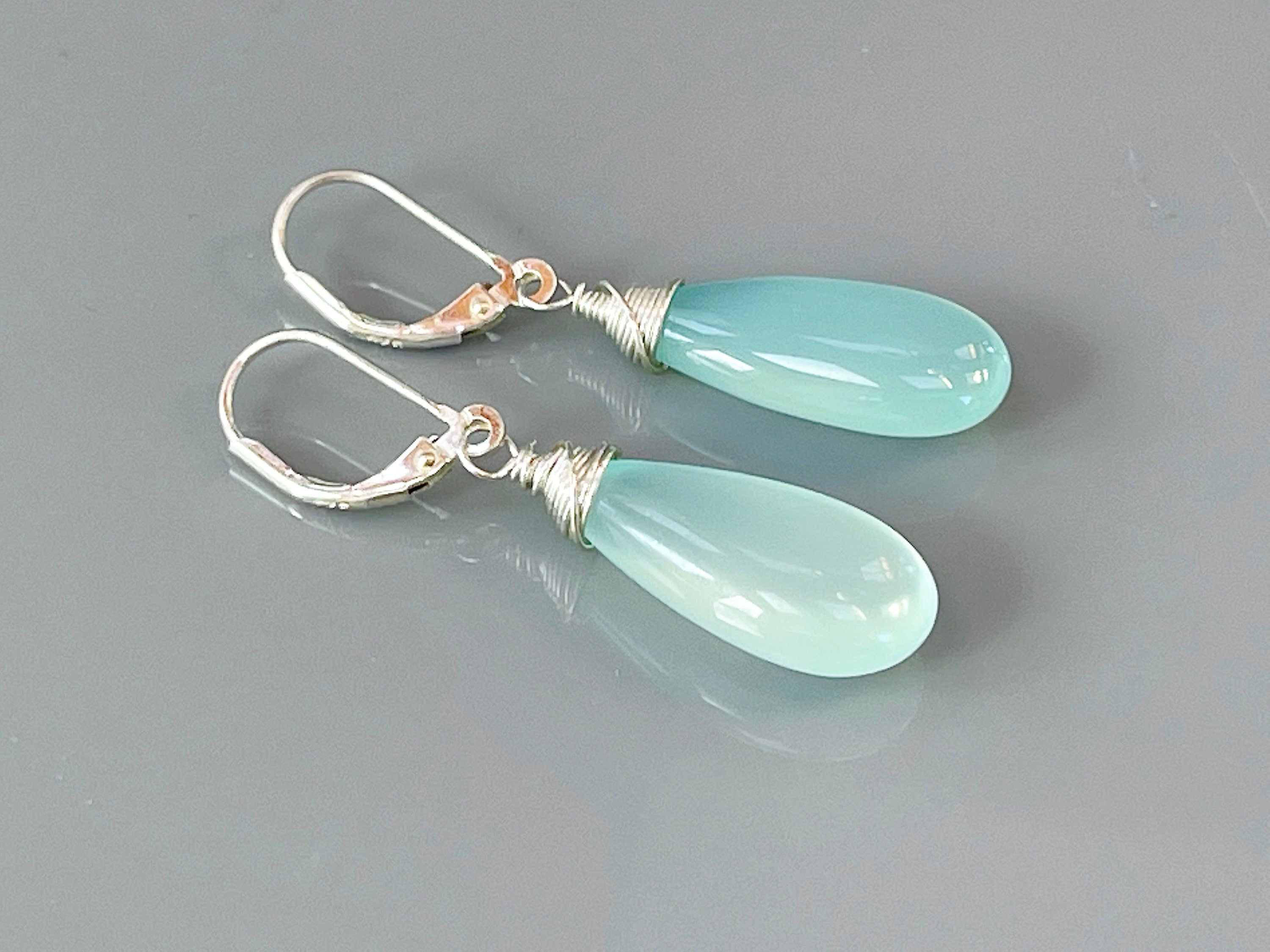 May include: A pair of silver teardrop earrings with light blue gemstone drops. The earrings have a wire wrapped design and a lever back closure.