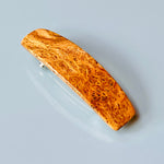 May include: A brown and gold wood hair clip. The clip is rectangular with rounded edges and features a unique wood grain pattern. The wood has variations in shades of brown and gold, creating a natural, marbled effect.  The clip is made of polished wood and has a sleek, modern design. This stylish hair accessory is perfect for adding a touch of natural elegance to any hairstyle.