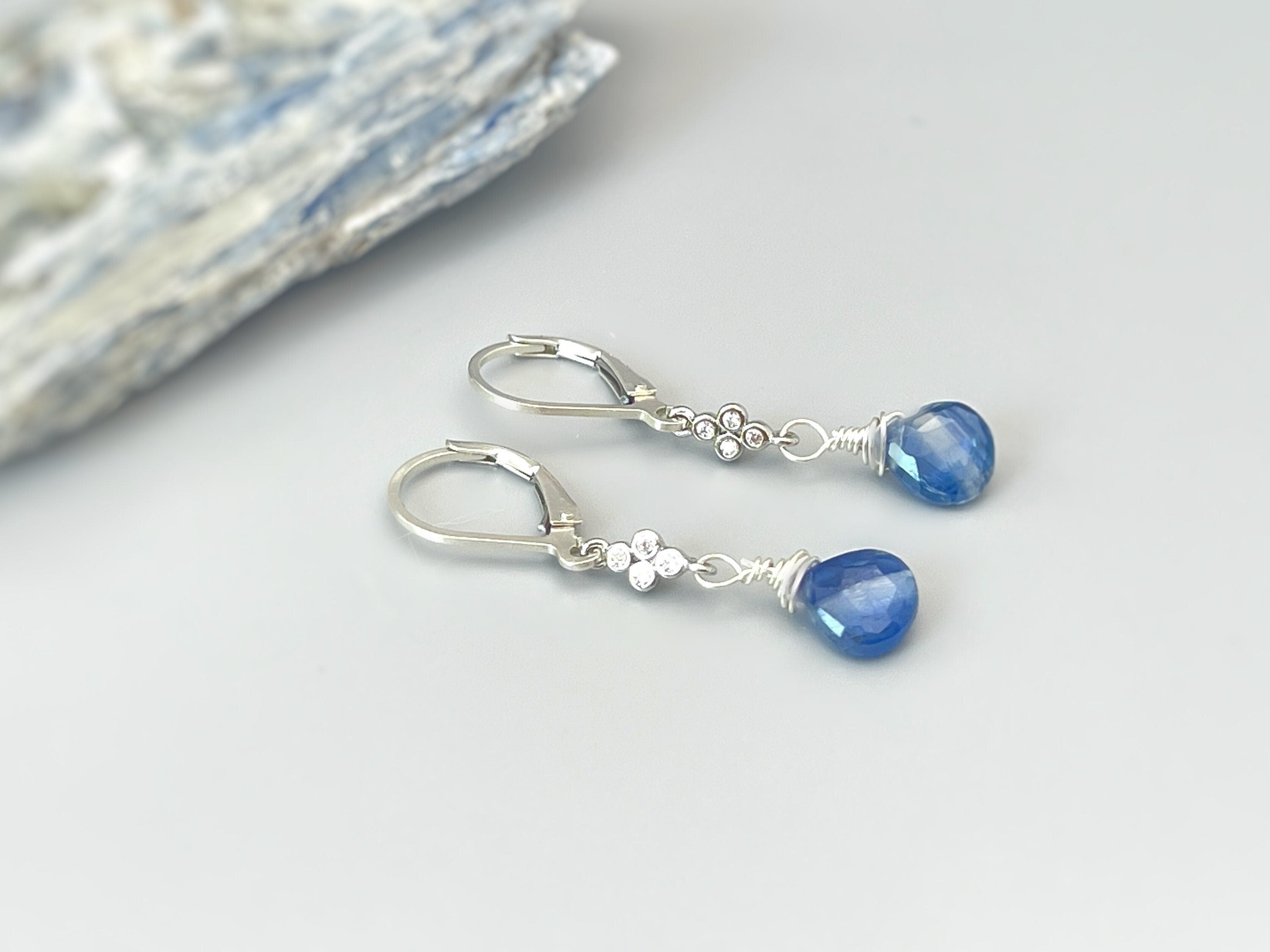 May include: Silver dangle earrings with blue teardrop shaped stones and a cluster of small clear stones