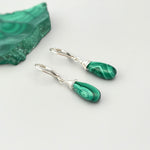 May include: A pair of silver dangle earrings with green malachite teardrop shaped stones. The stones have a swirling pattern.