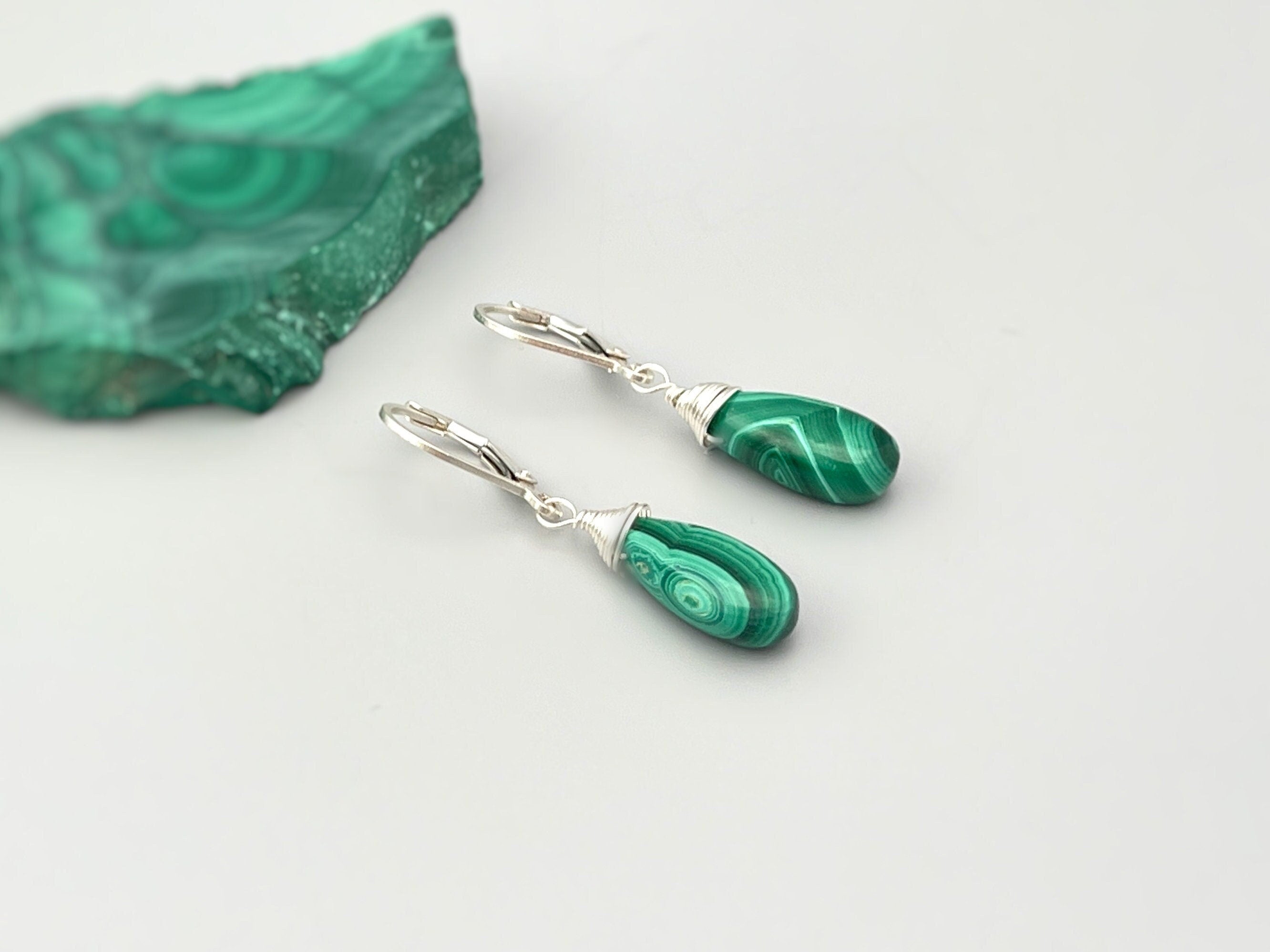 May include: A pair of silver dangle earrings with green malachite teardrop shaped stones. The stones have a swirling pattern.