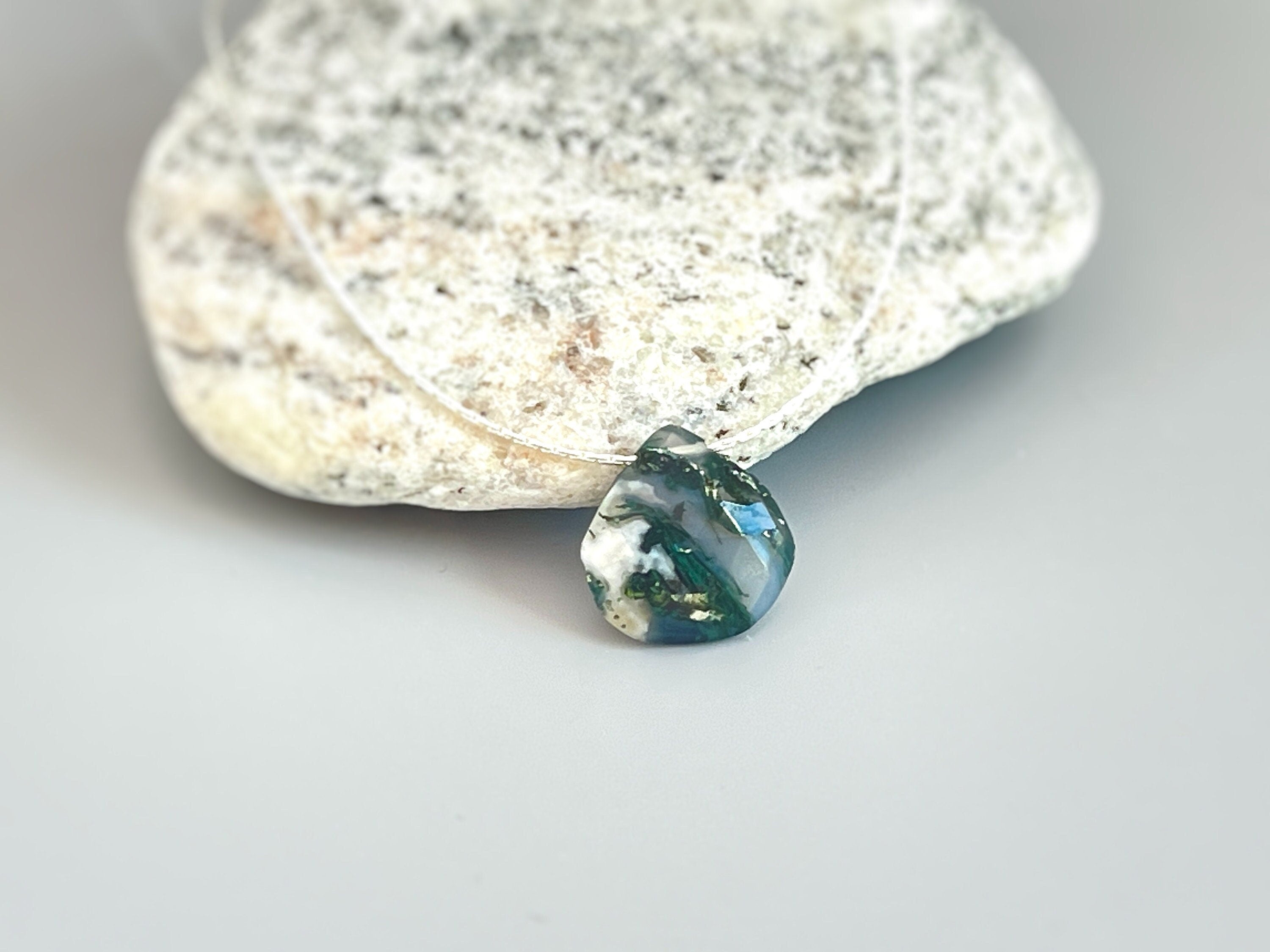 May include: A green, white, and black agate gemstone pendant on a clear string necklace.