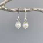 May include: A pair of silver dangle earrings with a single white pearl on each earring.