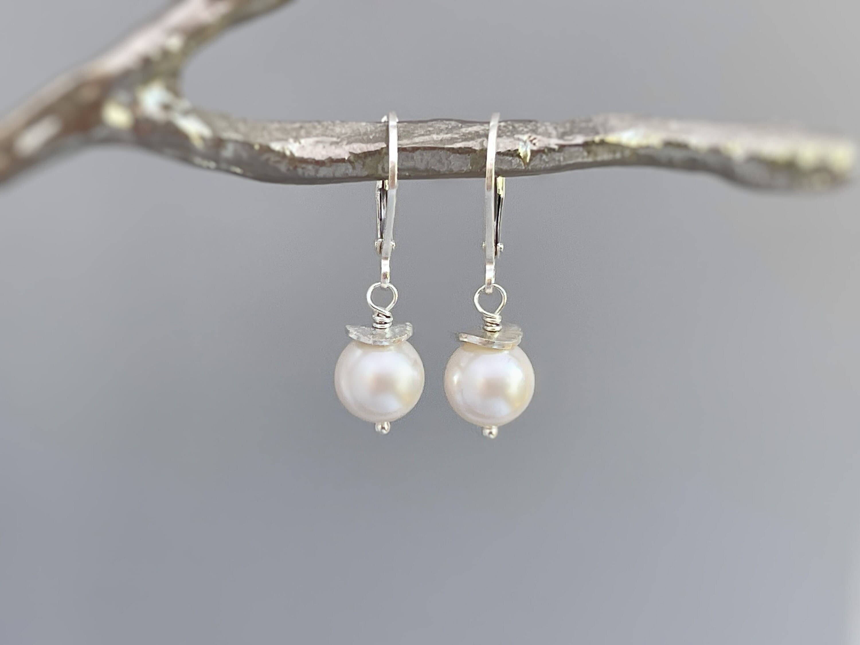 May include: A pair of silver dangle earrings with a single white pearl on each earring.