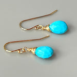 May include: A pair of gold earrings with turquoise teardrop shaped stones. The stones are faceted and have a bright blue color. The earrings are simple and elegant.
