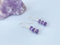 May include: A pair of silver dangle earrings with three faceted amethyst gemstones on each earring.