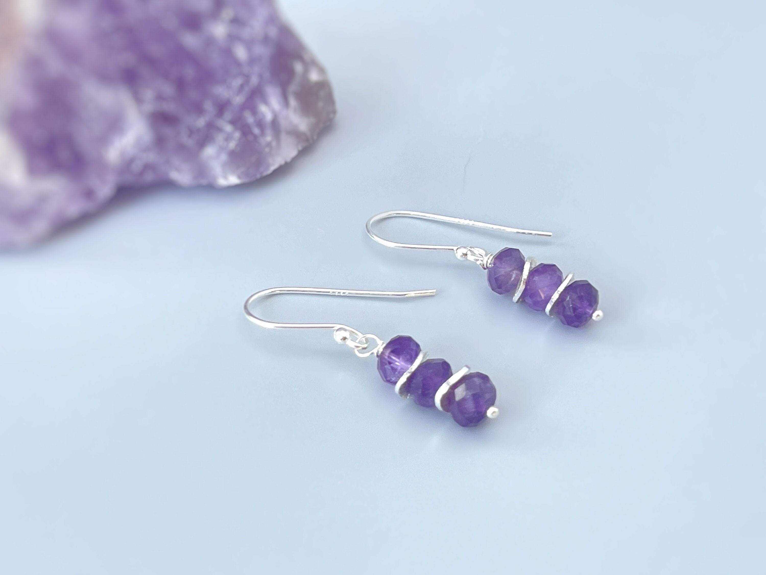 May include: A pair of silver dangle earrings with three faceted amethyst gemstones on each earring.