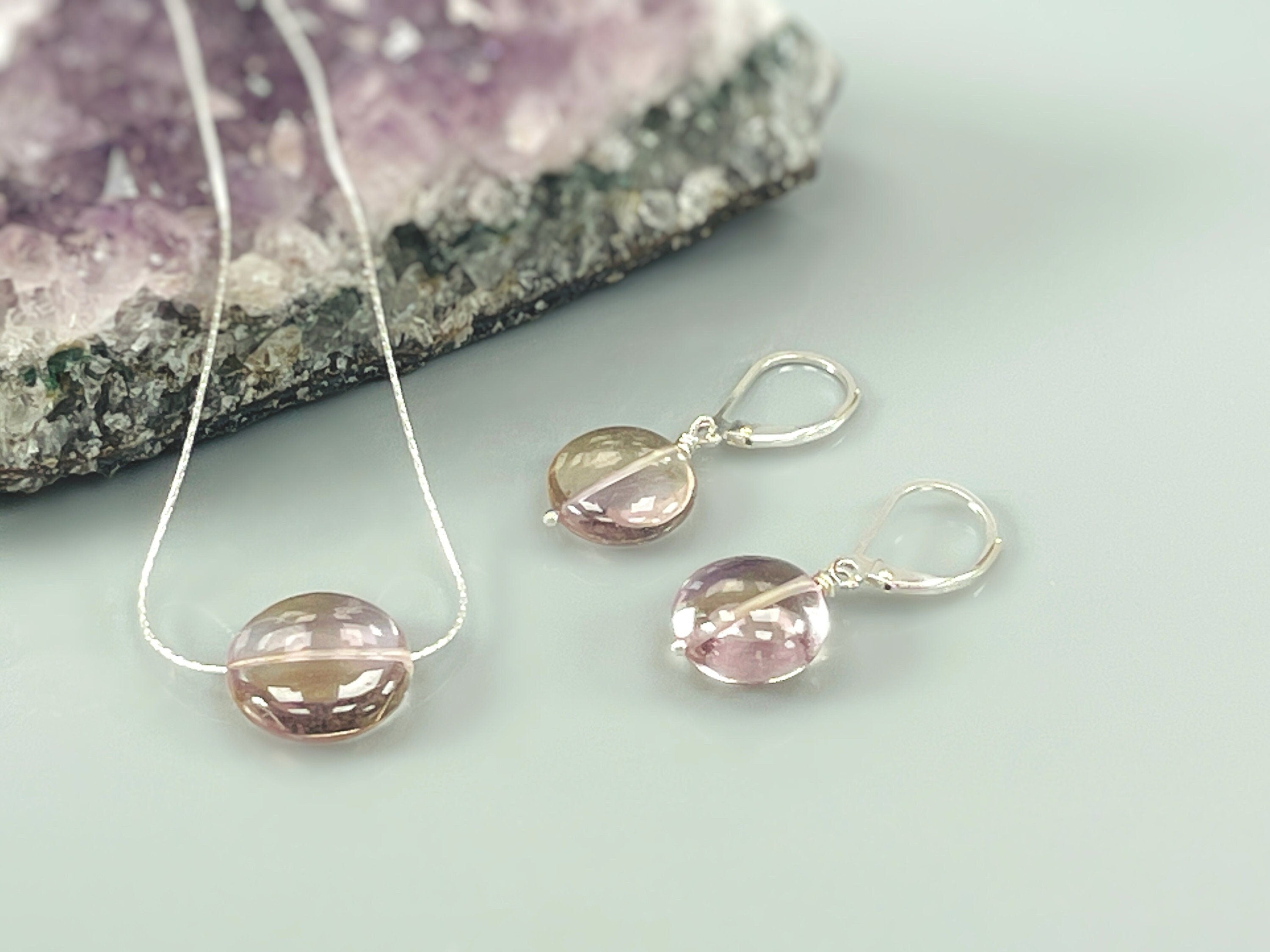 May include: A silver necklace and earrings set with a round, pink and brown gemstone pendant and matching earrings.