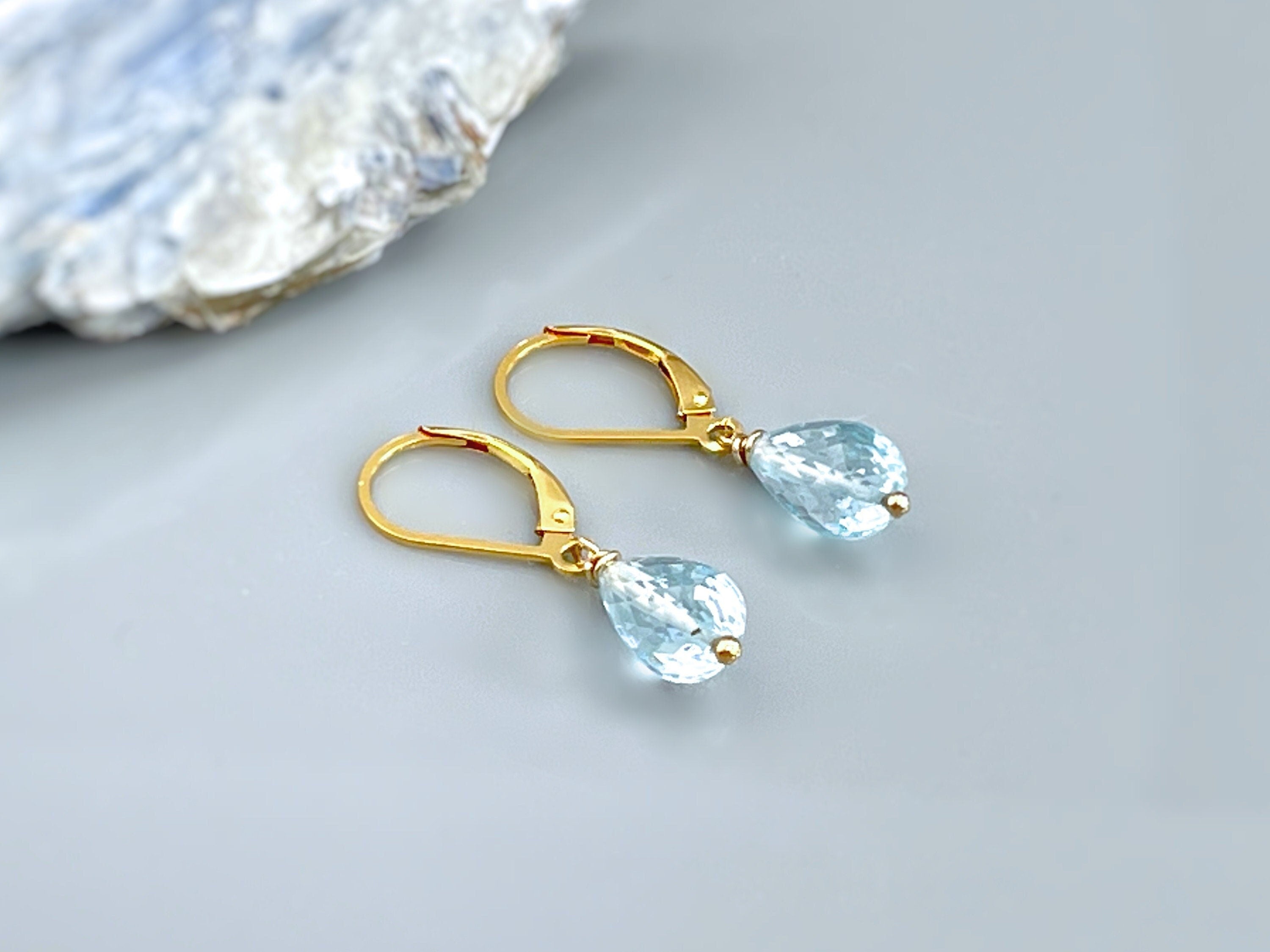 May include: A pair of gold teardrop earrings with light blue gemstone accents.