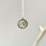 May include: A silver necklace with a round pendant featuring a green and white agate stone set in a silver filigree frame.