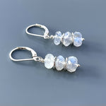 May include: Silver dangle earrings with three faceted moonstone beads each. The moonstone beads are a light white color with a slight iridescent sheen.