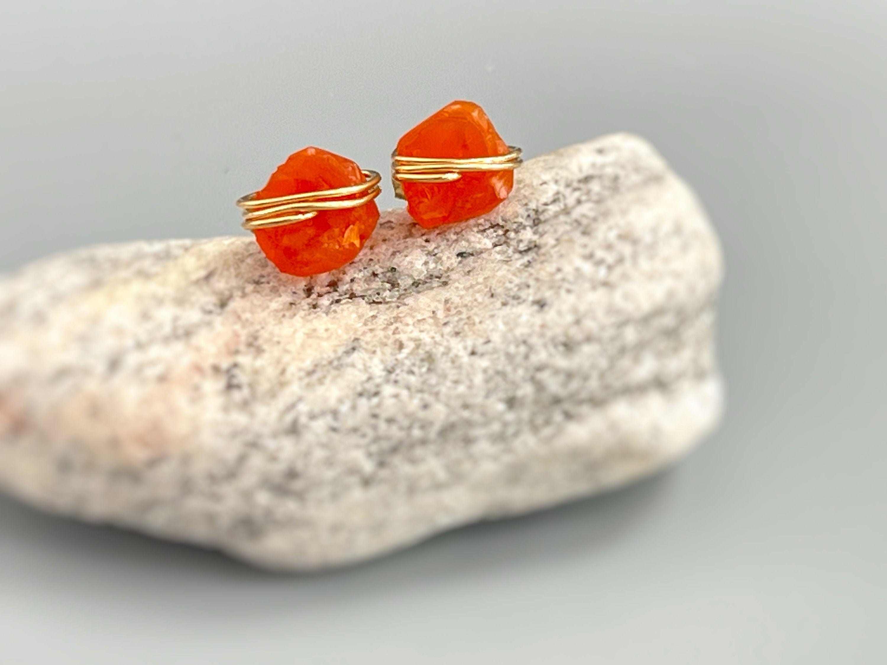 May include: Two orange gemstone earrings with gold wire wrapped around them