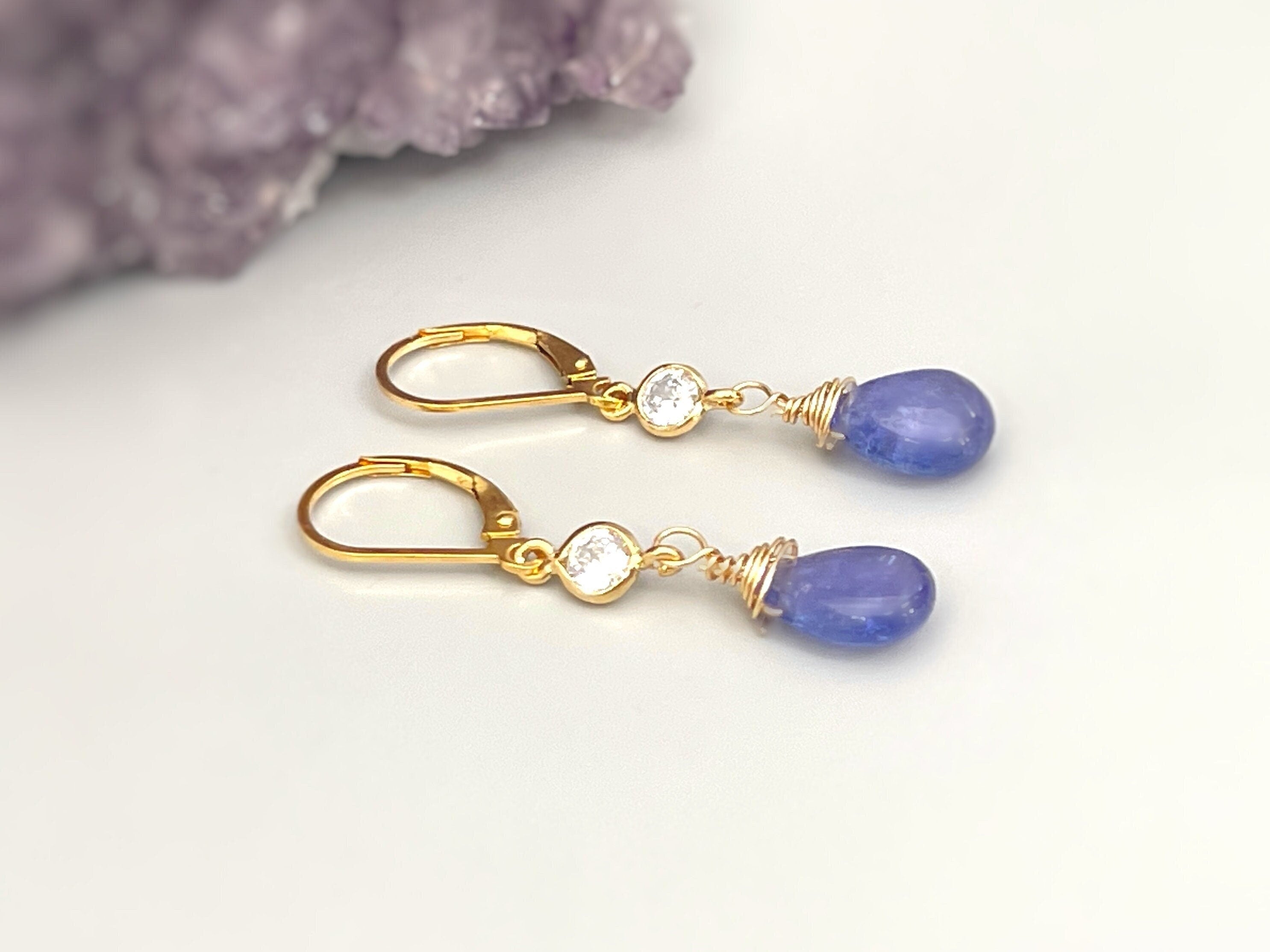 May include: Gold teardrop earrings with a small clear stone accent. The teardrop stones are a light blue color.