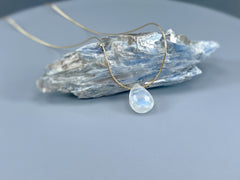 May include: A teardrop-shaped moonstone pendant necklace on a gold chain. The pendant is white with a blue iridescent sheen.