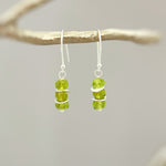 May include: Silver dangle earrings with three green peridot gemstones on each earring.