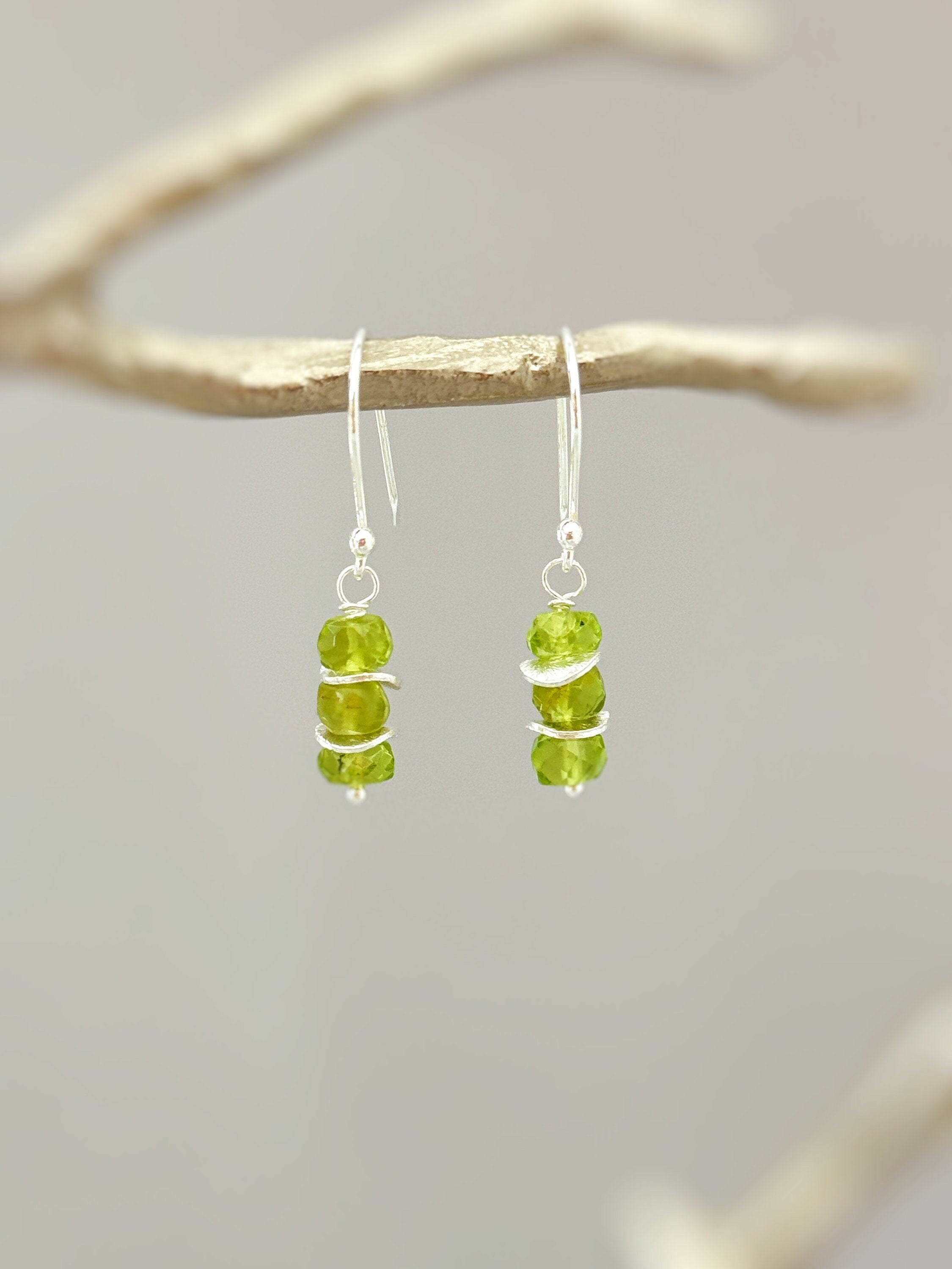 May include: Silver dangle earrings with three green peridot gemstones on each earring.