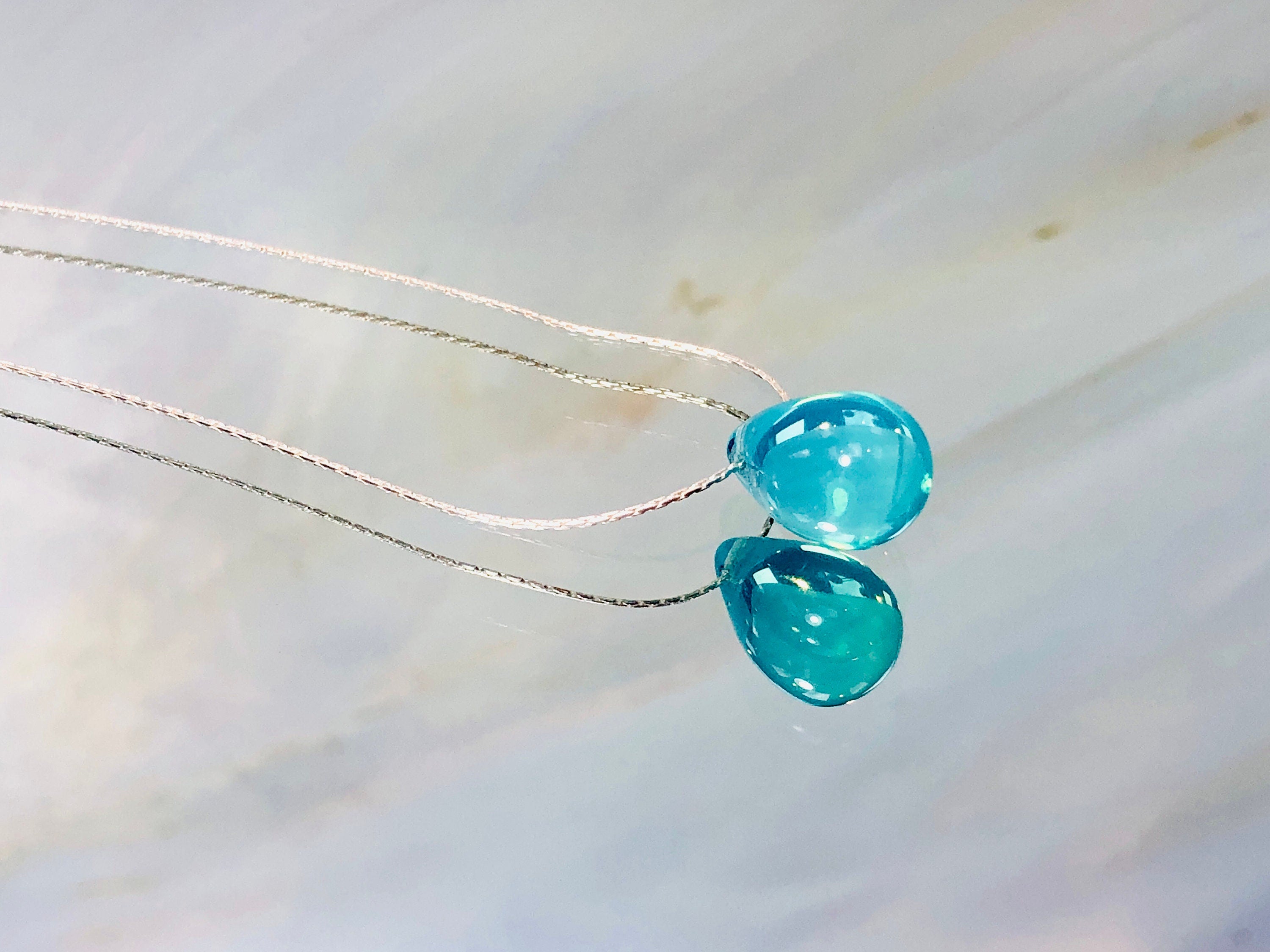 May include: A silver chain necklace with a teardrop shaped light blue pendant