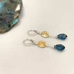 May include: A pair of silver dangle earrings with a teardrop shaped blue gemstone and a round, yellow gemstone on each earring.