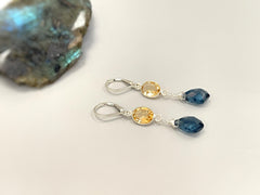 May include: A pair of silver dangle earrings with a teardrop shaped blue gemstone and a round, yellow gemstone on each earring.